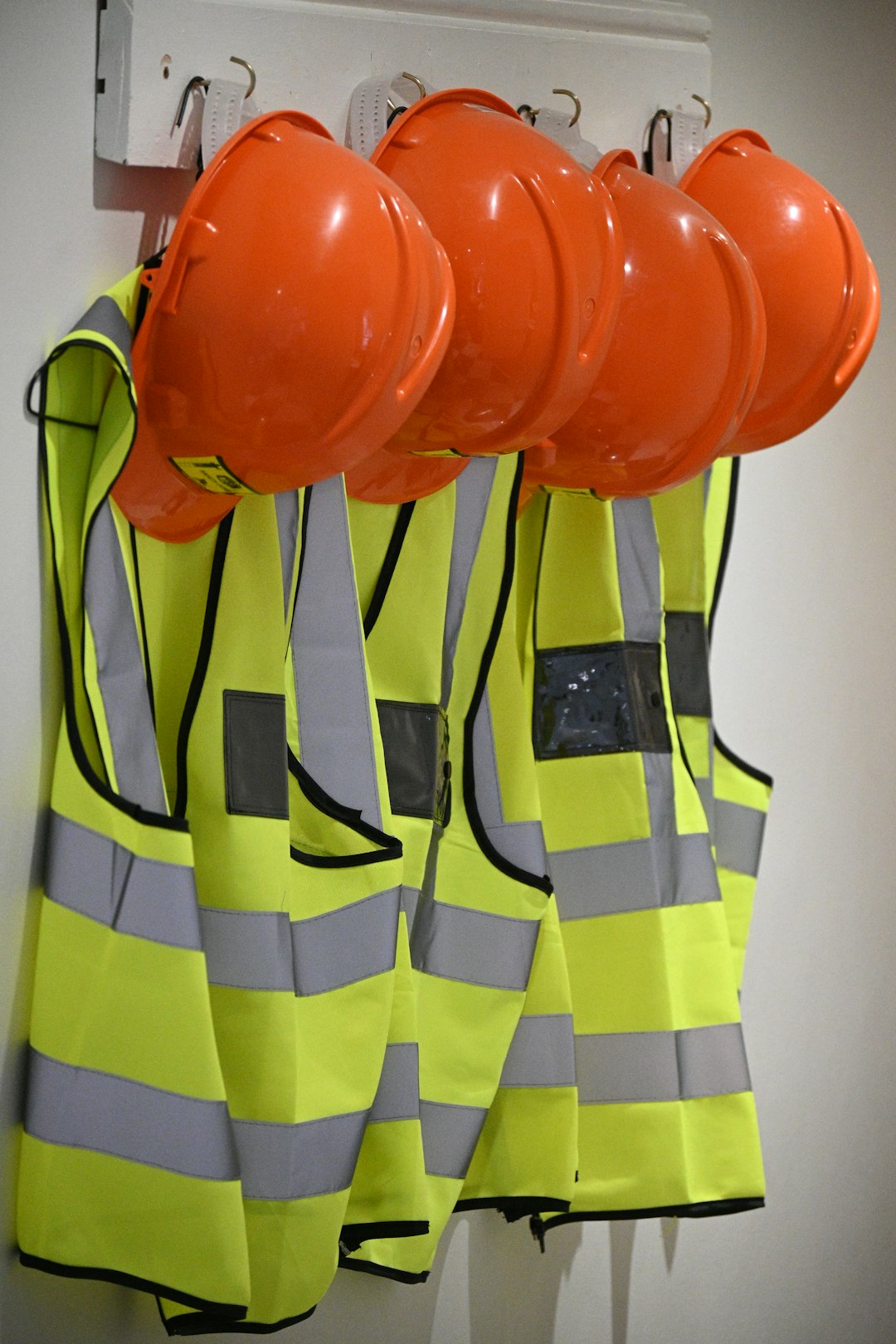 Four orange hard hats and neon yellow safety vests hanging on a wall