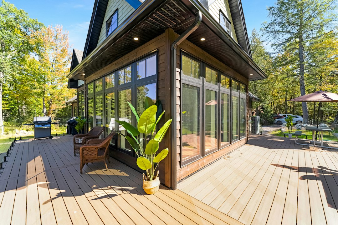 A wooden deck with wicker chairs and a potted plant beside a house